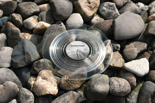 Transparent vinyl record mockup displayed on natural rocks, top-down perspective with sunlight and shadows.