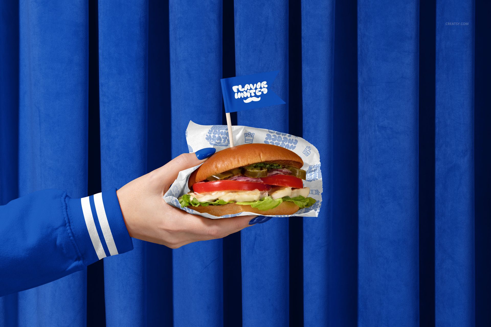 PSD mockup showing a hand presenting a wrapped vegan burger with branding, set against a bold blue curtain backdrop.