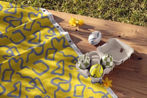PSD mockup showing patterned cotton fabric in yellow and blue beside a carton of colorful Easter eggs on wood.