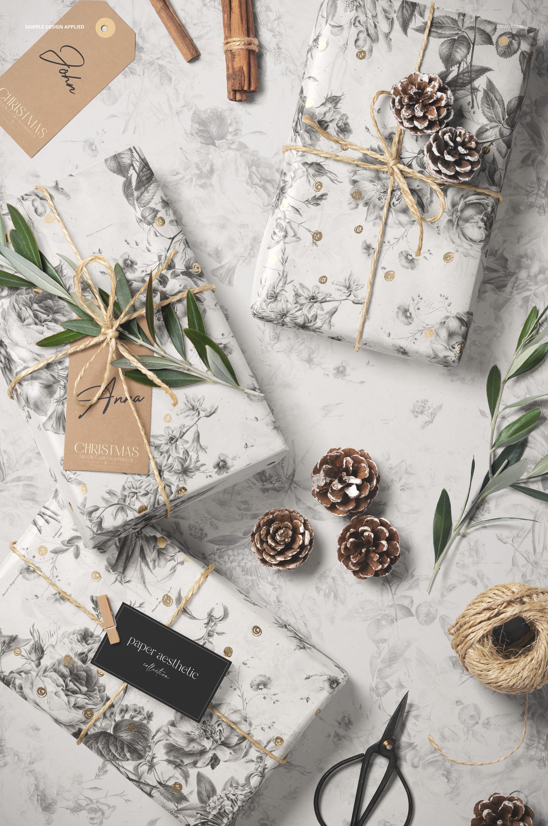Christmas gift wrapping mockup featuring white paper with olive tree branch illustrations, pinecones, and twine from a top view.