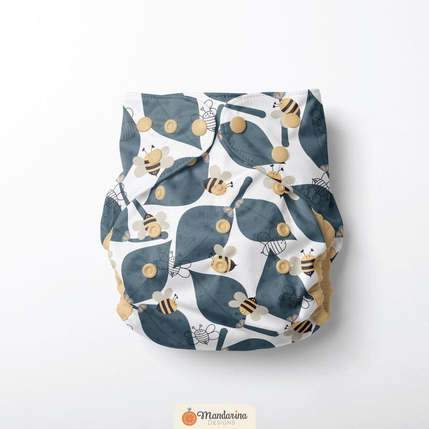 Reusable baby cloth diaper mockup featuring a playful bee and leaf pattern in blue, yellow, and white on a plain background.