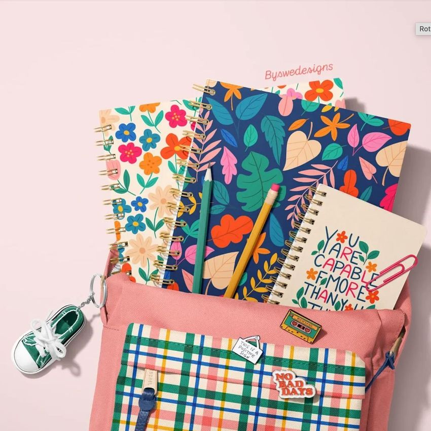 School backpack mockup with spiral notebooks featuring colorful floral and leaf patterns, pencils, and a sneaker keychain.