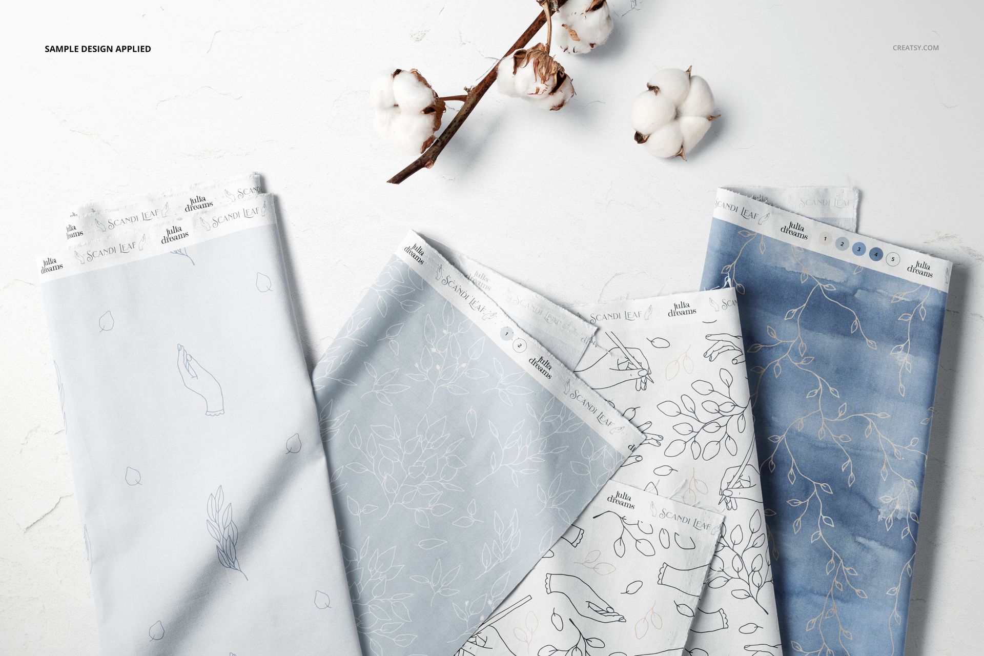 Folded fabric pieces in soft blue and white tones with minimal line patterns, arranged on a white surface.