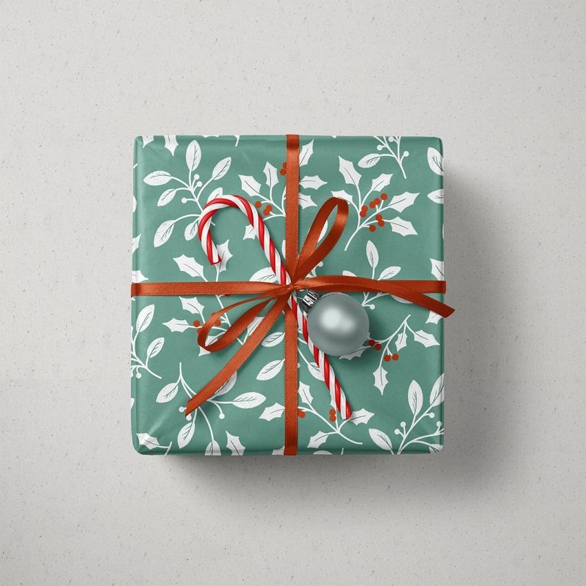 Christmas gift mockup featuring a green box with white holly leaf pattern, tied with a red ribbon, candy cane, and silver ornament.