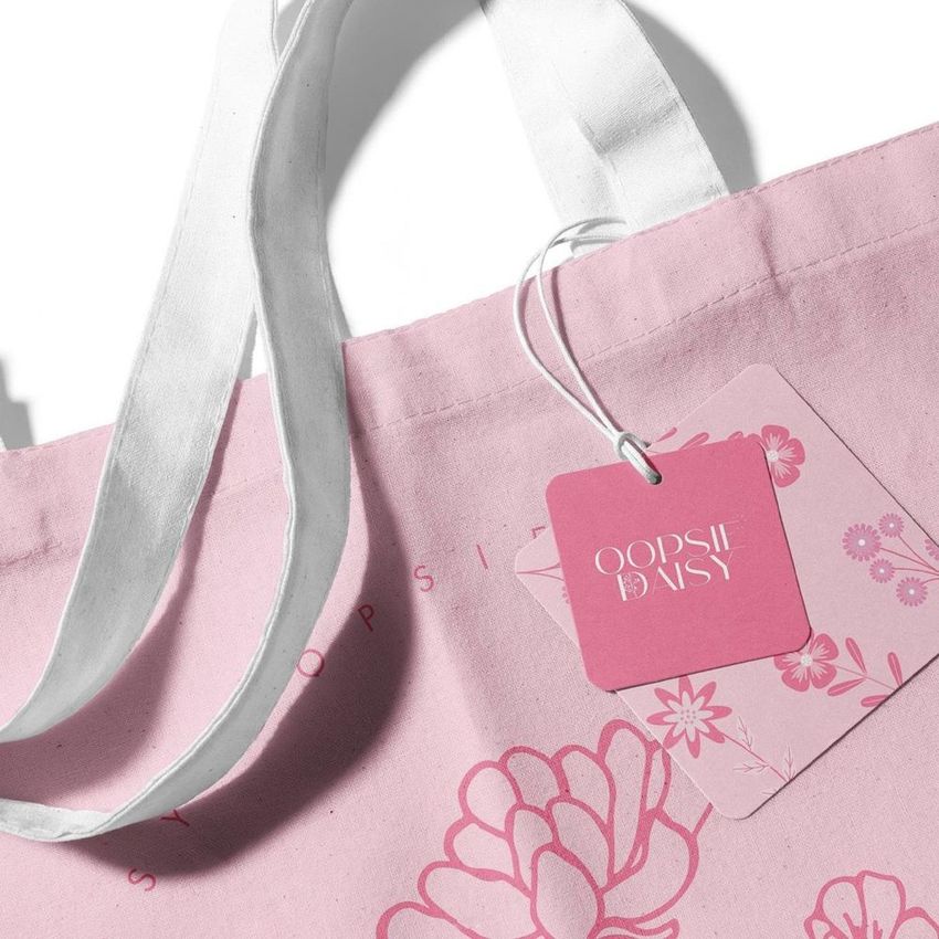 Canvas tote bag mockup featuring a close-up of white handles and a pink tag with floral graphics on a light pink background.