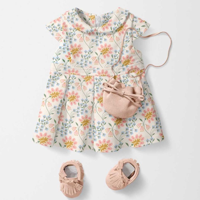 Baby dress mockup with a Peter Pan collar, featuring a pastel floral pattern, displayed with matching pink shoes and a small bag.