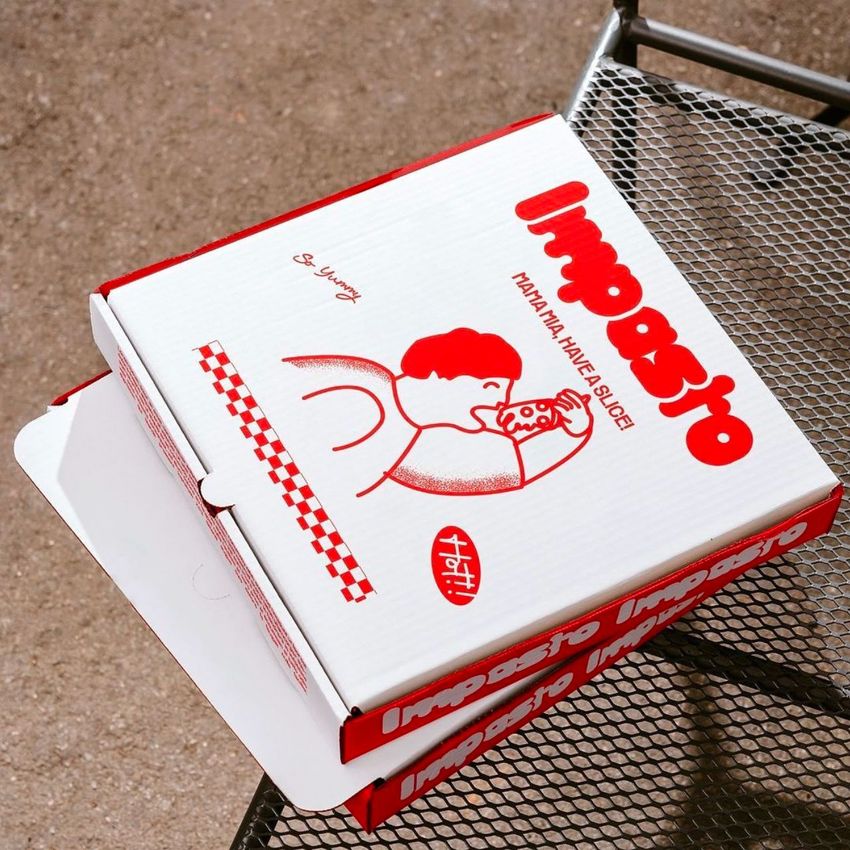 Pizza box mockup with red and white design featuring an illustration of a person eating pizza, placed on a metal outdoor table.