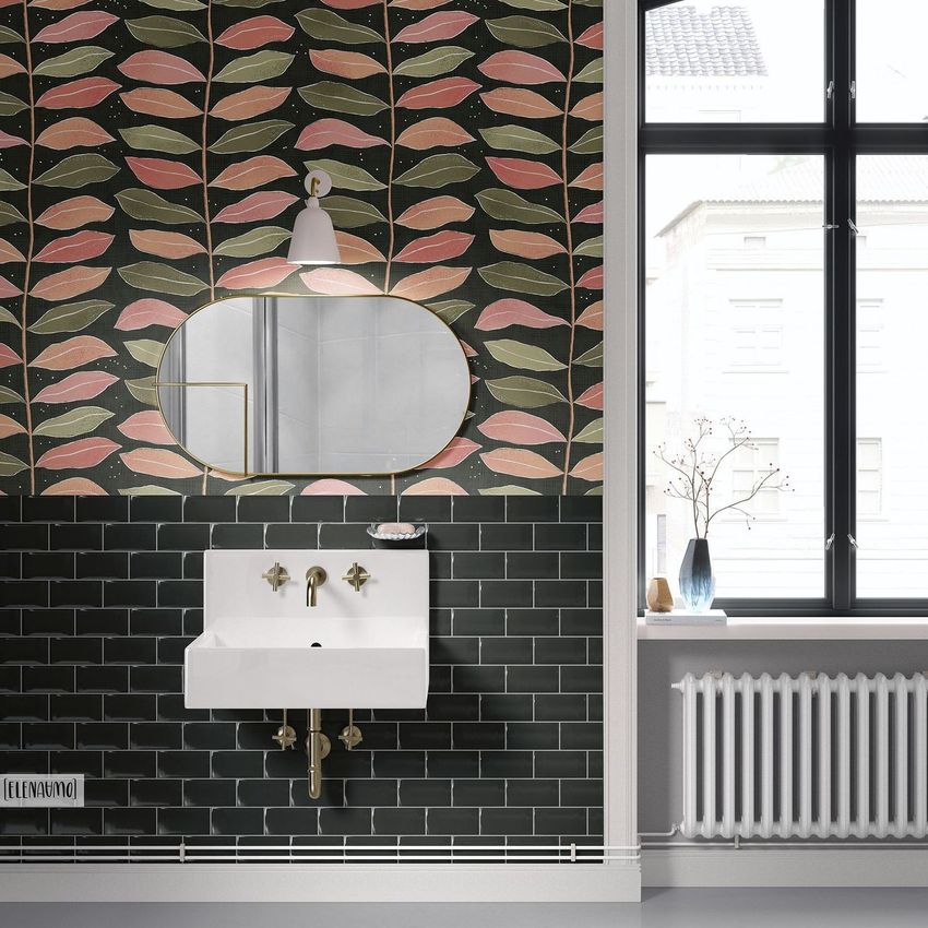 Vintage bathroom mockup featuring a patterned wallpaper with pink and green leaves above dark subway tiles, a white sink, and an oval mirror.