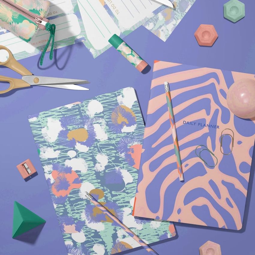 Stationery mockup featuring two A4 notebooks with colorful abstract and zebra patterns, surrounded by office supplies on a purple surface.