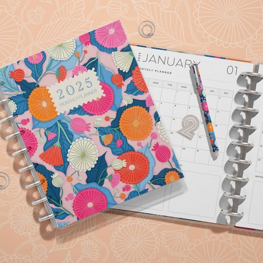 Stationery mockup showing a floral-patterned planner cover and an open planner displaying a calendar and pen on a patterned surface.