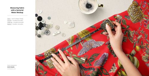 Hands measuring a red fabric with botanical and fruit patterns using a measuring tape, surrounded by buttons and a cup of coffee.