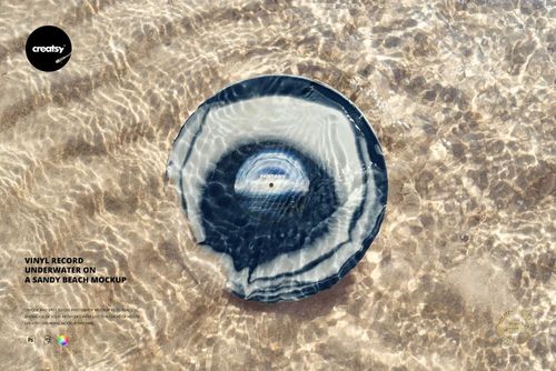 PSD mockup showing a vinyl record lying on a sandy beach, surrounded by shallow water and shimmering reflections.