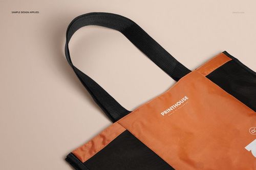 Front view of a mesh shopping tote bag mockup with black handles and orange body, displayed on a beige surface.