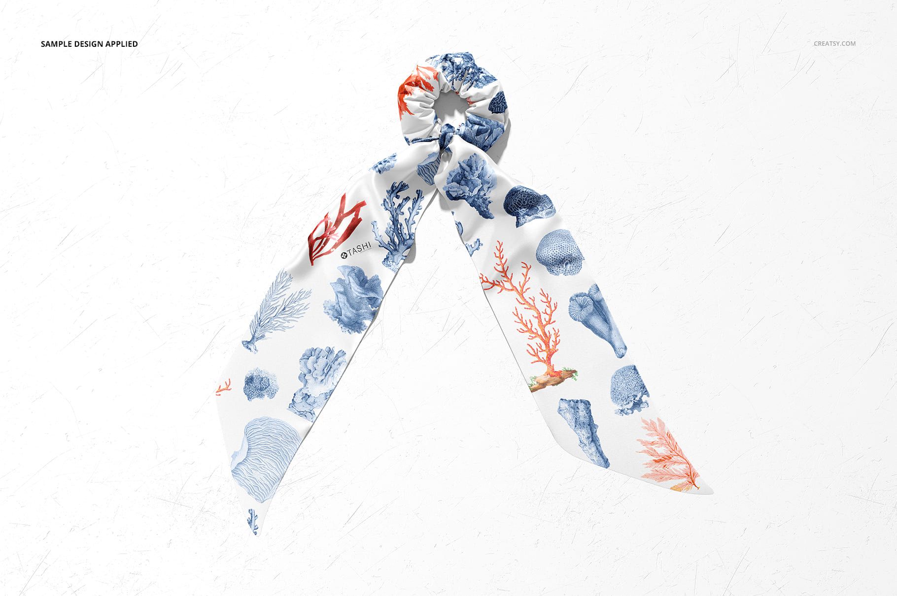 Fashion accessory mockup showing a scrunchie scarf with sea-inspired blue and red coral motifs on white fabric.