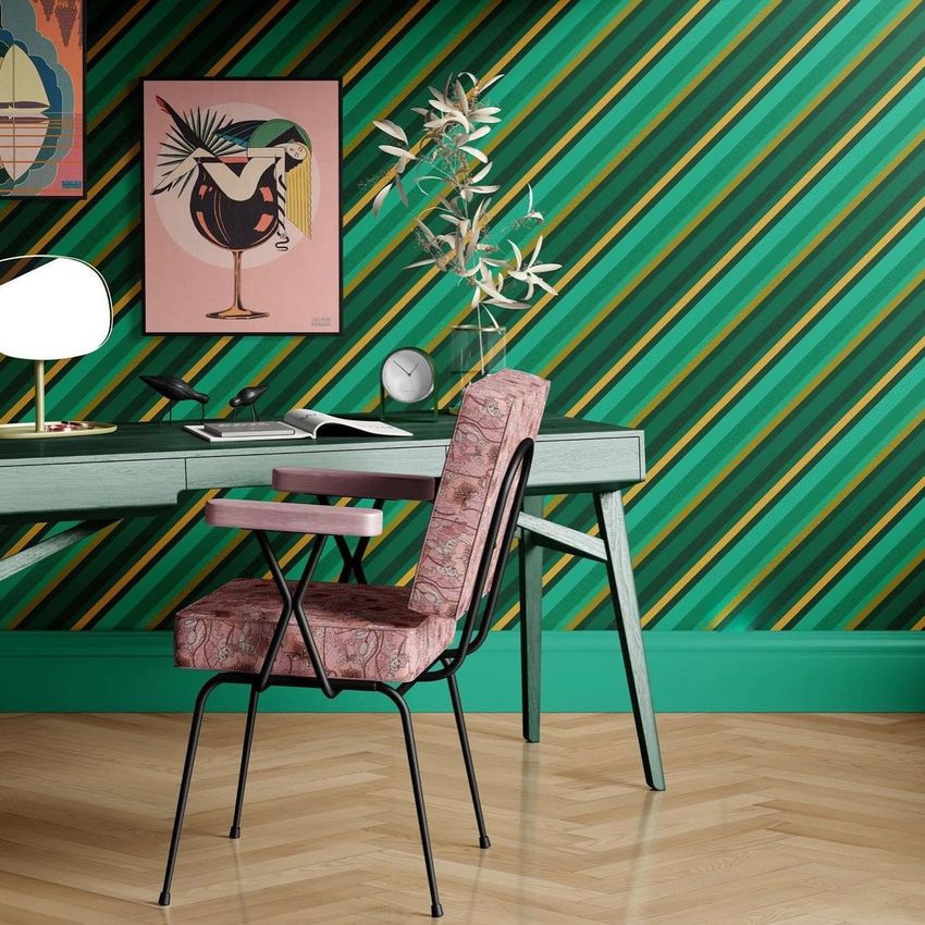 Interior scene with a green and black striped wallpaper, a desk mockup, a patterned chair, and framed artwork on the wall.