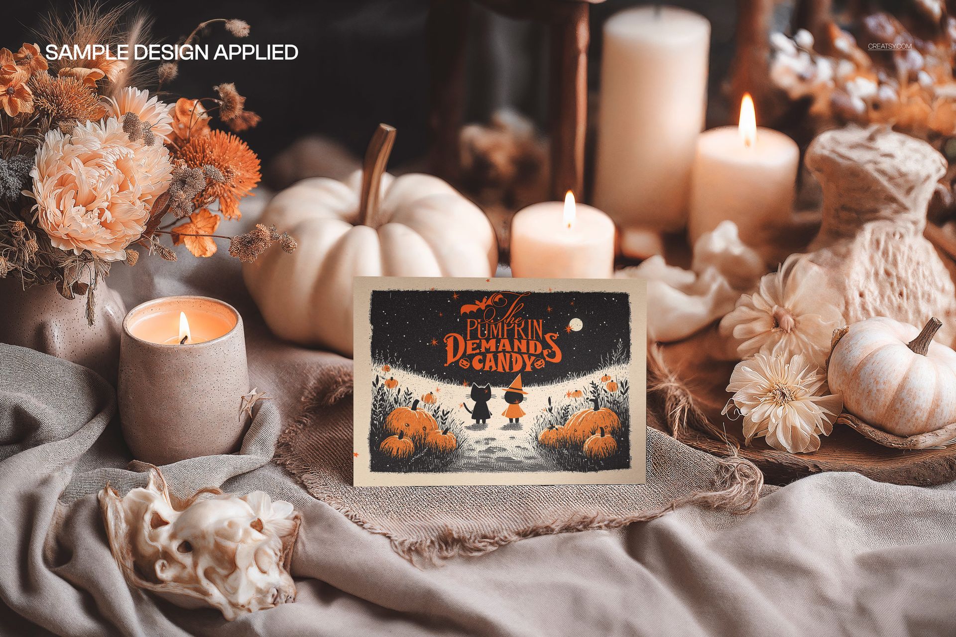 Halloween greeting card mockup on beige fabric with pumpkins, candles, and autumn flowers in a cozy scene.