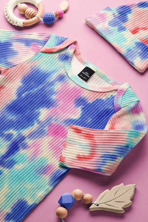 Baby ribbed gown and hat mockup with blue, pink, and purple tie-dye pattern, arranged on a pink surface.