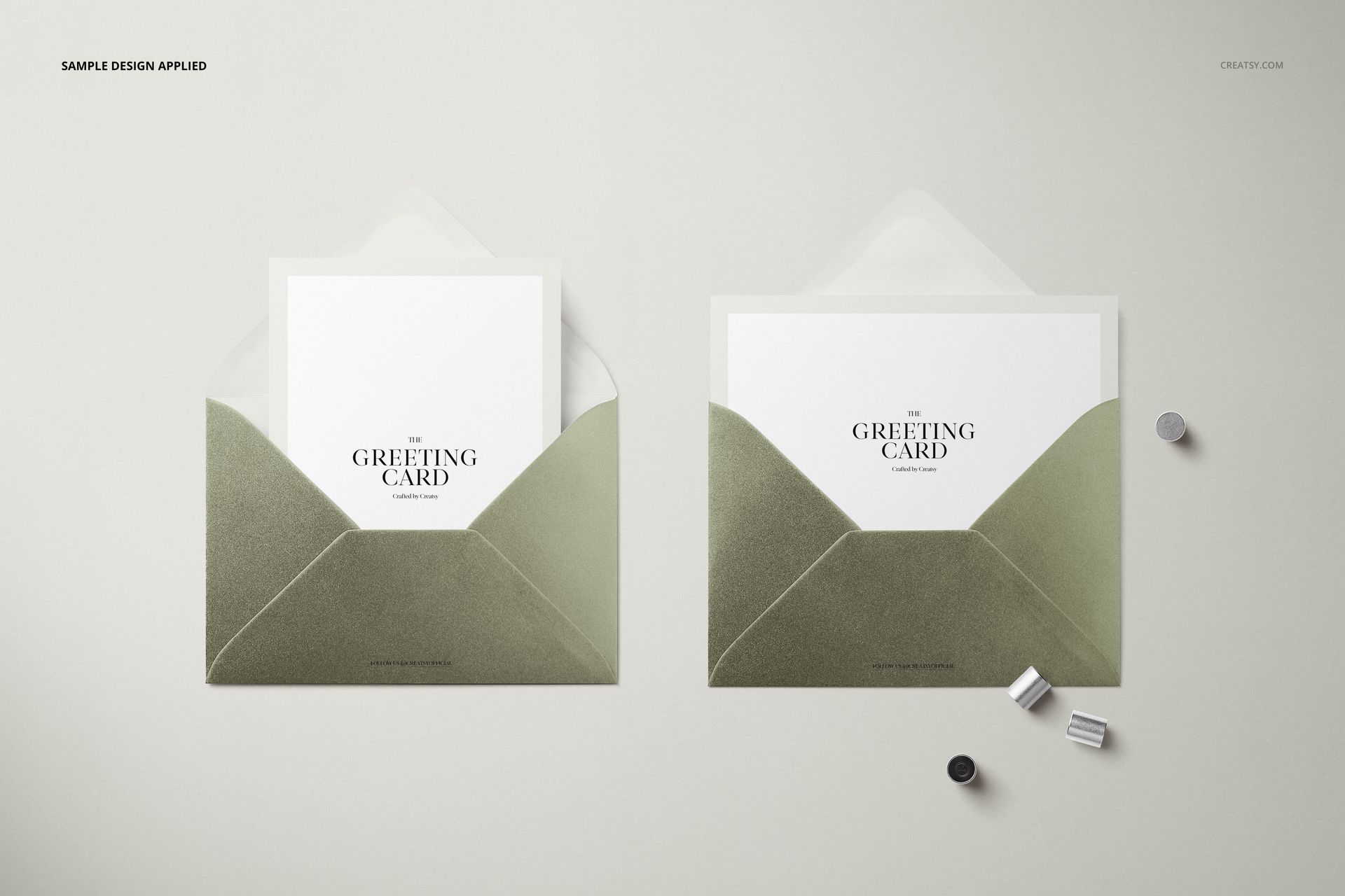 Mockup of two open C6 envelopes with greeting cards, metallic finish, displayed with small cylindrical objects on a pale background.