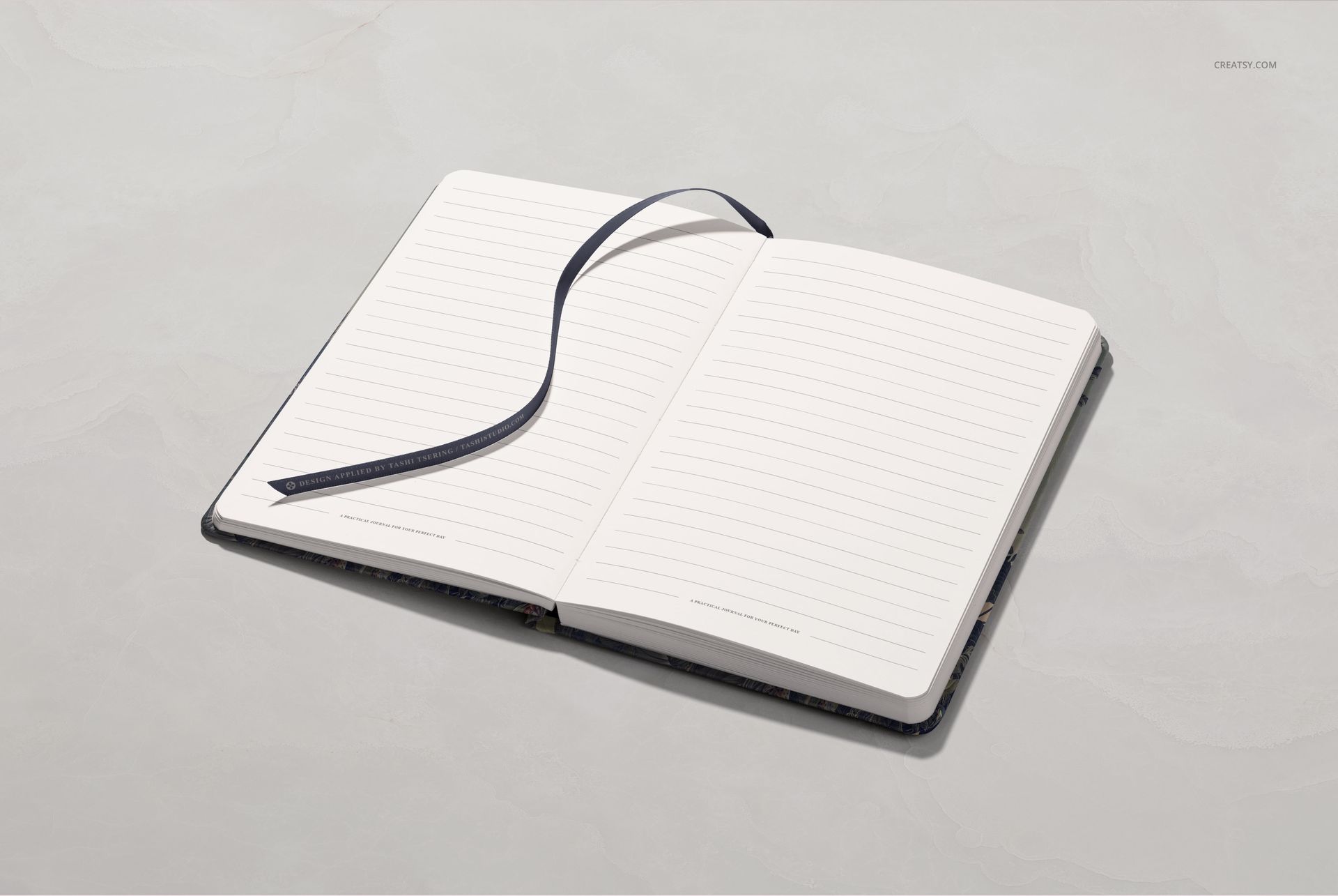 Leather notebook mockup displayed open with ruled pages and a dark ribbon, photographed from above on a neutral background.