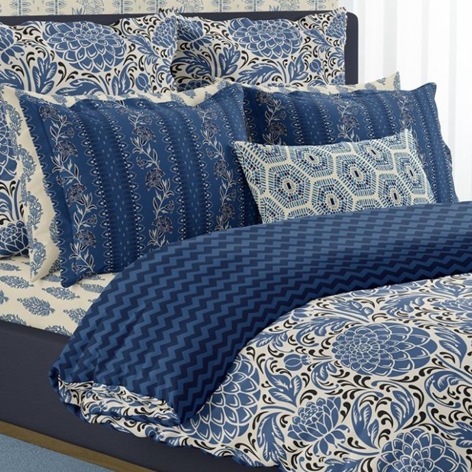Bedding mockup showing a bed with blue and cream floral and geometric patterned pillows, sheets, and duvet in a bedroom scene.