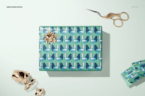 Gift wrapping paper mockup featuring a box with repeating abstract pattern, gold bow, scissors, and ribbon on a pale background.