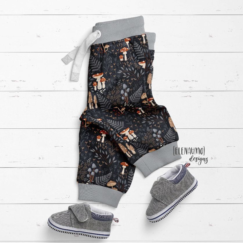 Baby sweatpants mockup featuring dark fabric with whimsical woodland patterns, styled with gray baby shoes on a white wooden surface.
