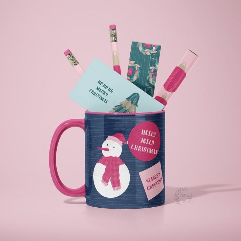 Mug mockup with a snowman illustration and holiday-themed cards and pencils arranged inside, set against a pink background.