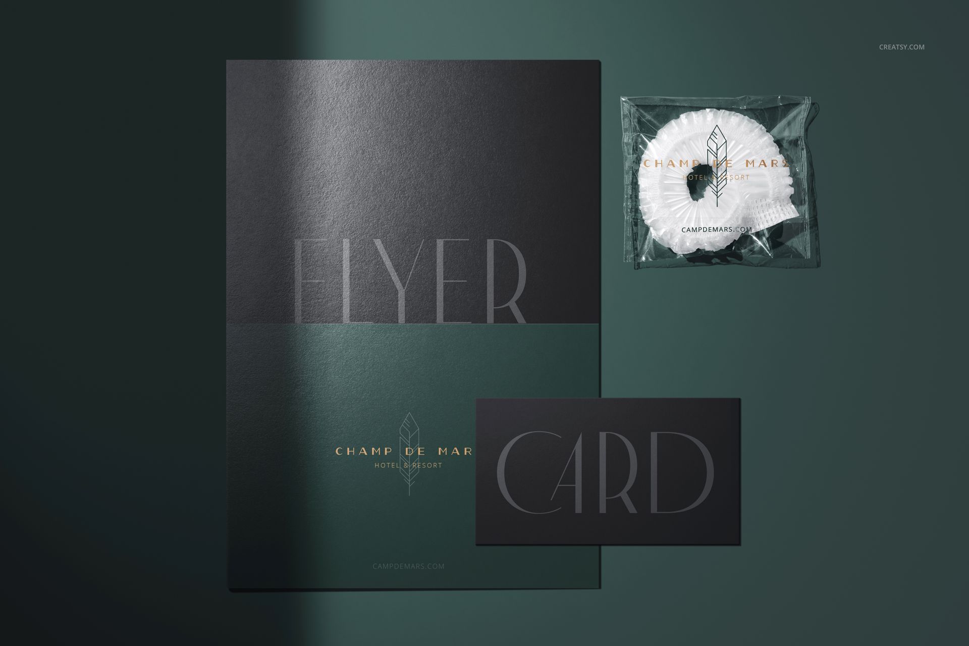 Top view of a hotel shower cap mockup in transparent wrapper next to a dark flyer and card on a green surface.