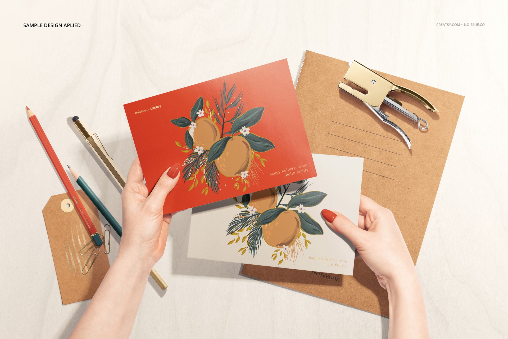 Top view of a stationery mockup scene with two illustrated cards, brown envelope, pencils, and a metal hole punch.