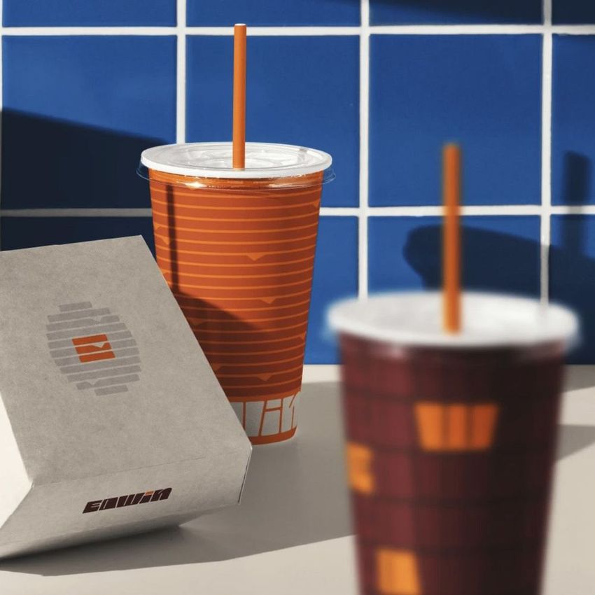 Burger packaging mockup featuring a striped orange drink cup and a white burger box on a light surface with blue tiled wall.