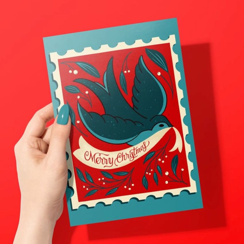 Greeting card mockup featuring a woman's hand holding a card with a festive bird illustration and holiday text on a red background.