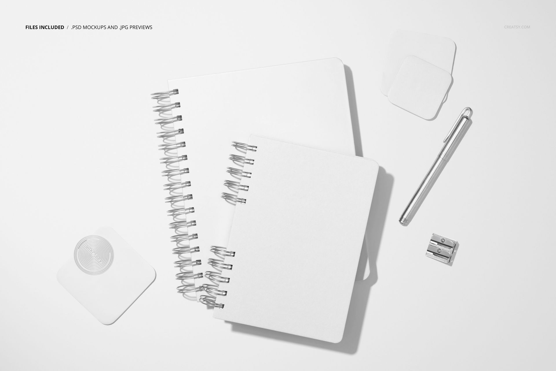 Stationery mockup showing two blank spiral planners, adhesive notes, pen, and sharpener from a top-down perspective.