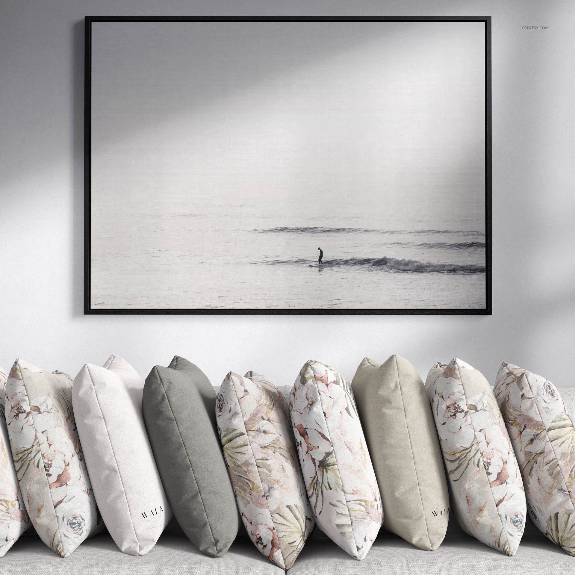 Neutral-colored pillows with floral and plain covers lined up in a row, PSD mockup, under a monochrome framed artwork.