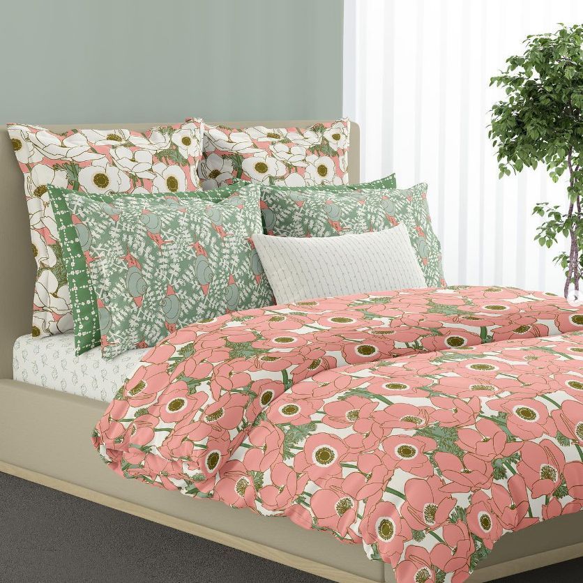 Bedding mockup featuring a floral and snail pattern on a duvet cover and pillows in a modern bedroom with a green wall and potted plant.