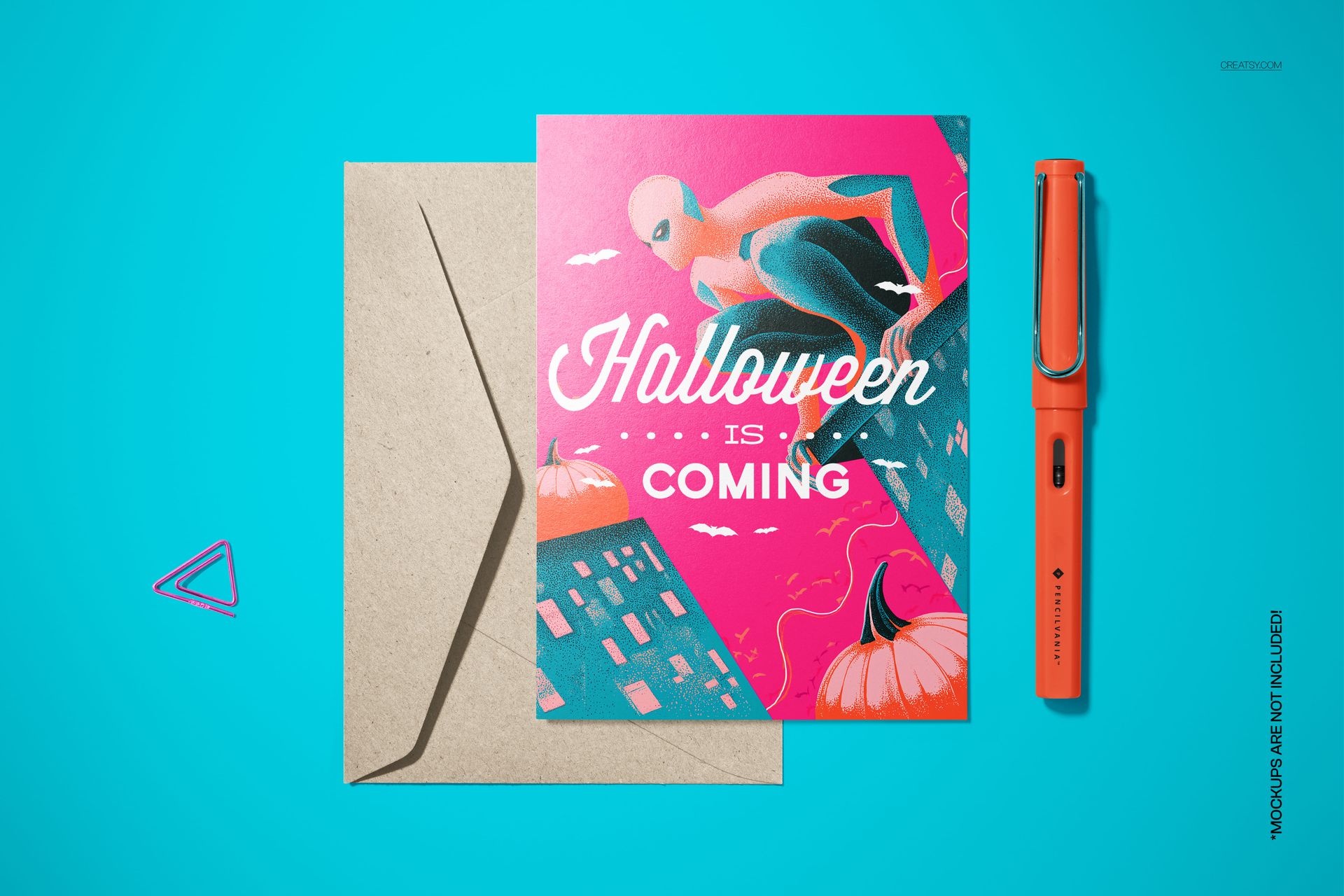 Halloween card mockup with a retro superhero illustration, placed beside a brown envelope and orange pen on blue background.