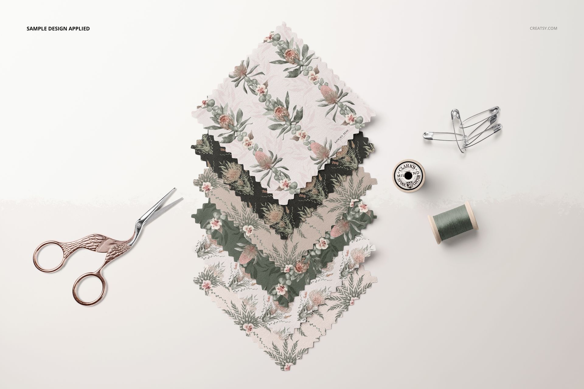 Fabric swatches mockup showing layered textiles with muted floral prints, viewed from above with scissors and thread.