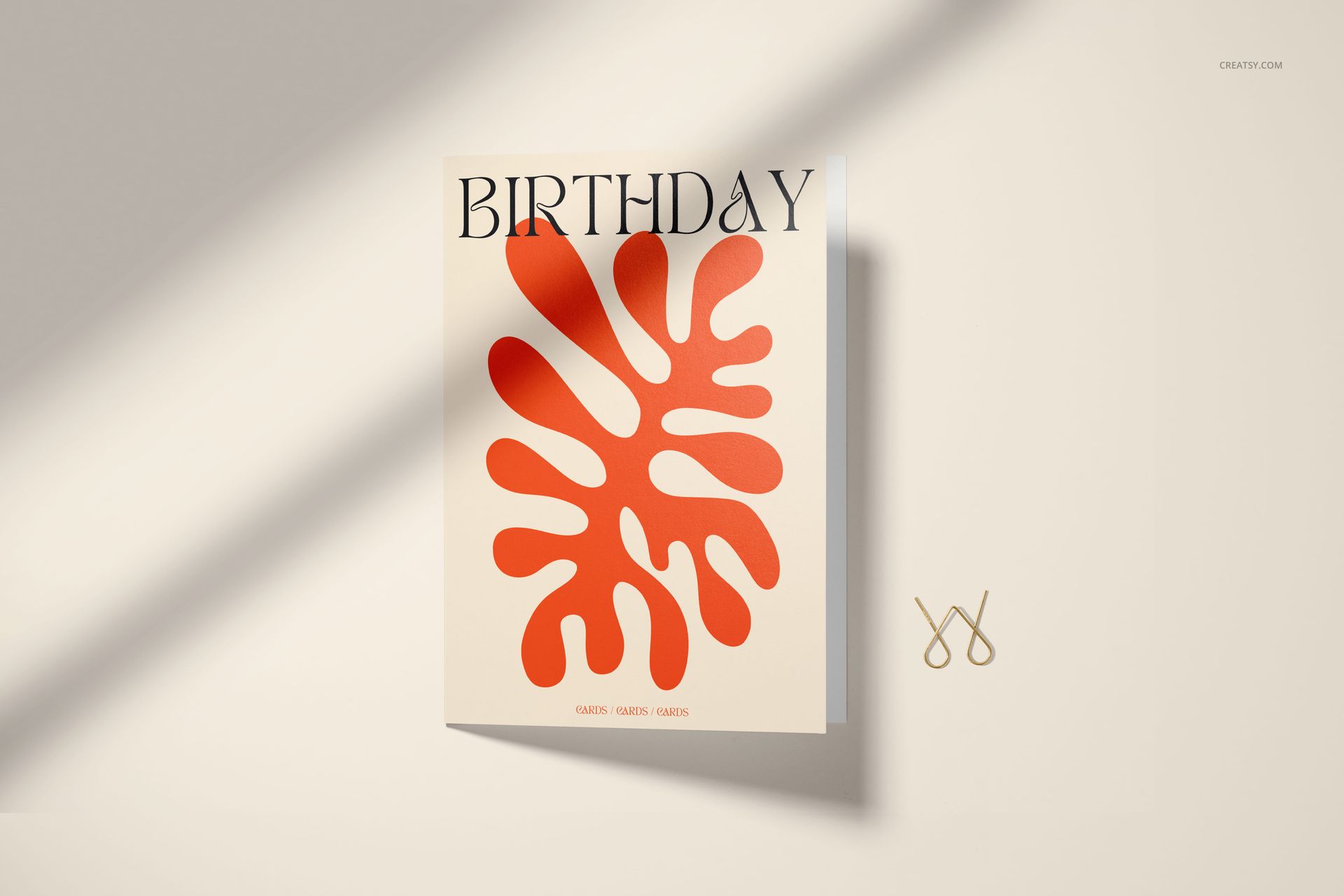 Front view of a 5x7 greeting card mockup with bold red abstract leaf design and large birthday text, on beige background.