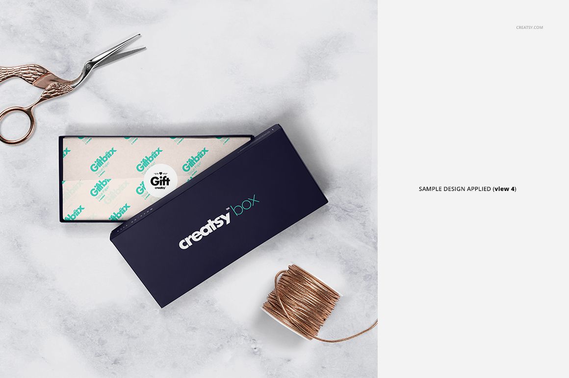 Top view of a gift box mockup set with white wrapping tissue paper, scissors, and copper ribbon spool on a white surface.