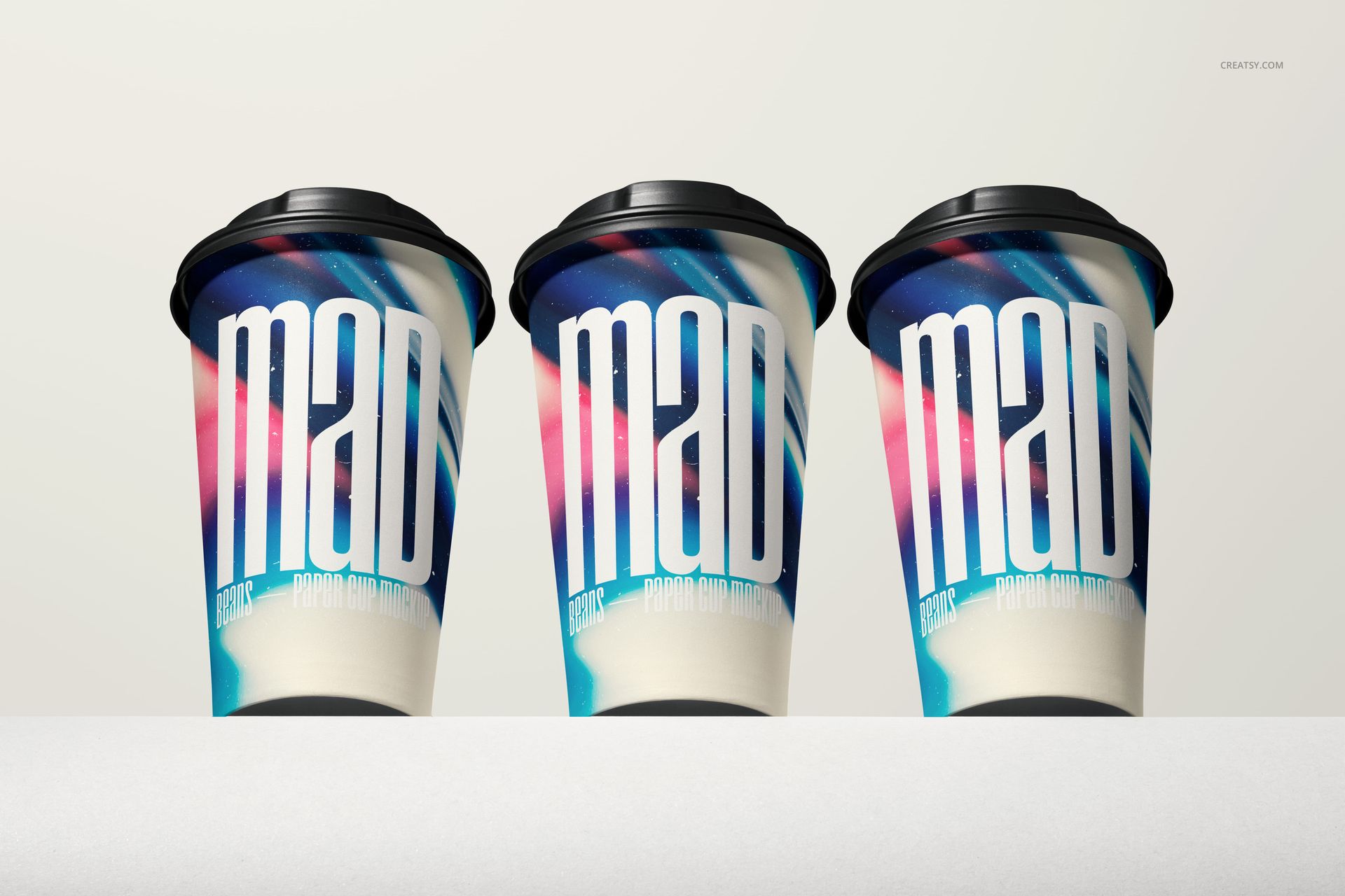 PSD mockup showing three paper cups with vibrant abstract artwork and black lids, placed on a light surface.