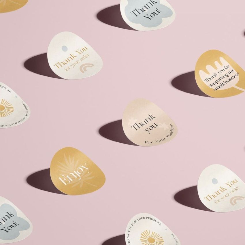Sticker mockup featuring various rounded stickers with thank you messages in muted pastel tones, arranged on a light pink surface.