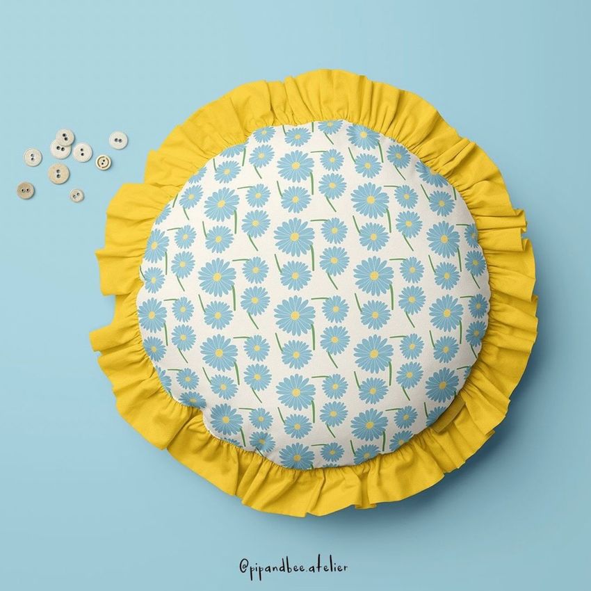 Round ruffled pillow mockup with a blue and white daisy pattern, yellow fabric border, and light blue background.