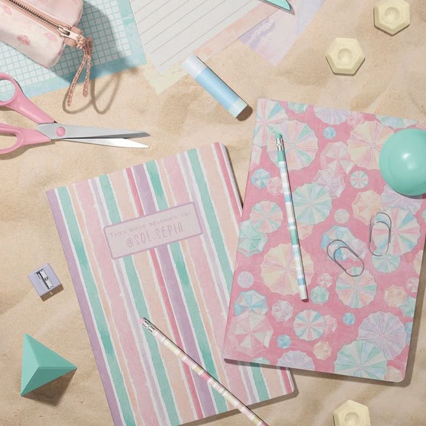 Stationery mockup featuring two classic A4 notebooks on a sandy surface, surrounded by pastel office supplies and geometric props.