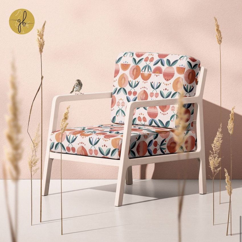 Lounge chair mockup with white wooden frame and cushions featuring a colorful fruit and floral pattern, set against a pale pink wall.