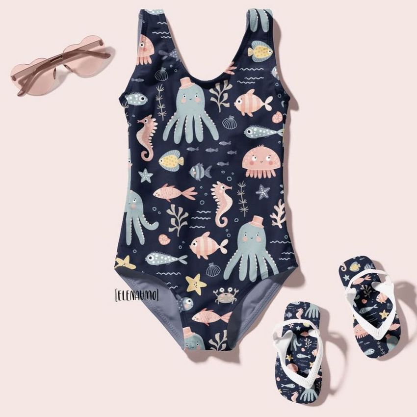 Baby swimsuit mockup featuring a navy blue one-piece with playful sea creature illustrations, paired with matching sandals and pink sunglasses.