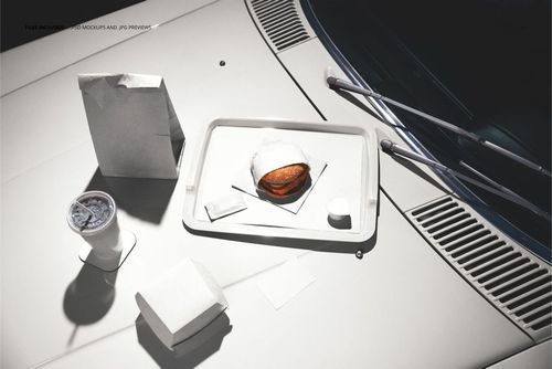 PSD mockup showing fast food items, including a burger, cup, and paper bags, placed on a white car hood.