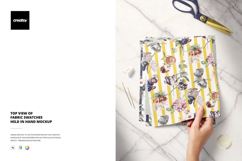 Top view of a hand holding several fabric swatches with floral and striped patterns, scissors and threads nearby.