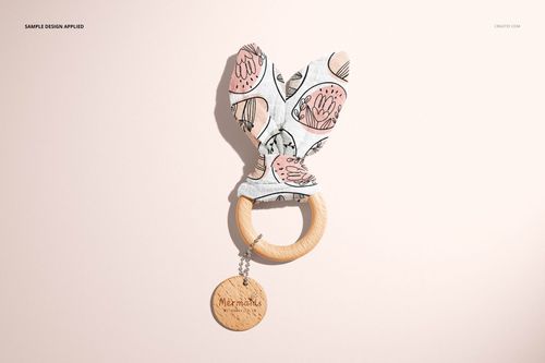 Top view of a wooden baby teether mockup with soft fabric ears in a pink floral print and round wooden ring.