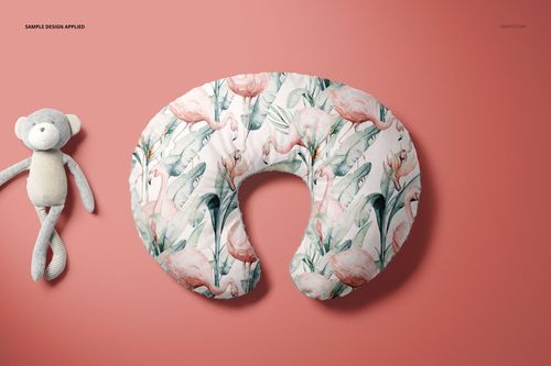 Mockup of a Boppy nursing pillow cover with a tropical flamingo design, displayed on a pink background beside a stuffed animal.