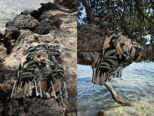 Mockup of a waffle beach towel featuring a botanical design, shown on rocks and hanging from a tree near the shore.