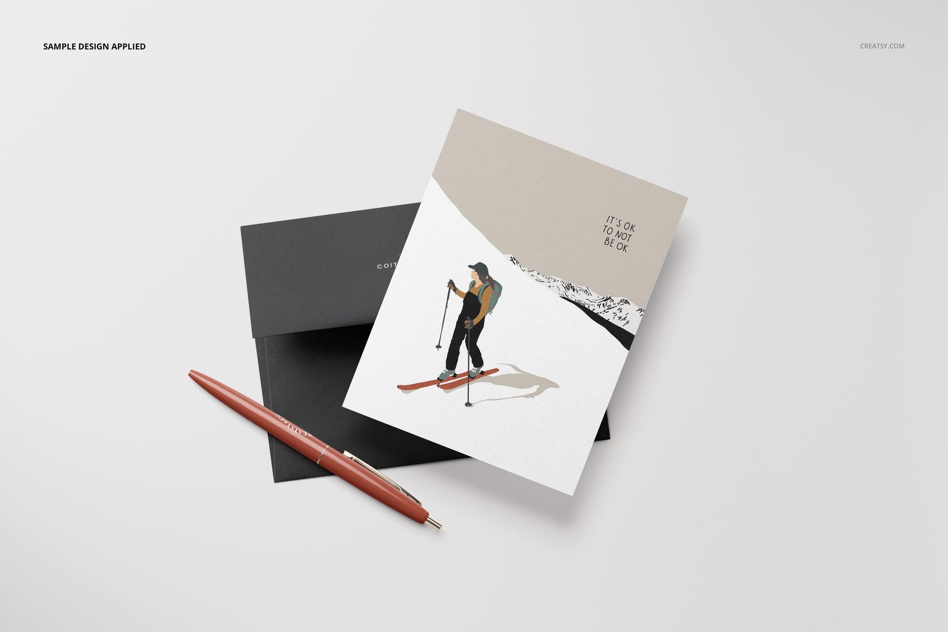 A2 card mockup with skier illustration and black envelope on a white surface, viewed from above with a pen nearby.